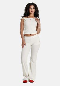 Witte geribbelde gebreide crop top met off-shoulder ontwerp, gecombineerd met bijpassende hoge taille flared broek. Rode logo-opdruk op beide stukken.