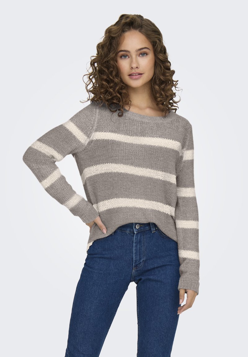 Suéter gris a rayas con amplias franjas crema, textura de punto y un corte relajado. Combinado con jeans de mezclilla oscuros de cintura alta.