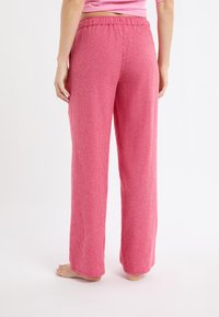 Różowe wzorzyste spodnie od piżamy z elastycznym paskiem, szerokimi nogawkami i miękką teksturą. Na tkaninie widoczny jest motyw w kratkę.