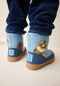 Blaue Kinderstiefel mit Cartoonfiguren, ausgestattet mit gepolstertem Material, Gummisohlen und einem strukturierten dunkelblauen Stoffbund am Hosenbein.