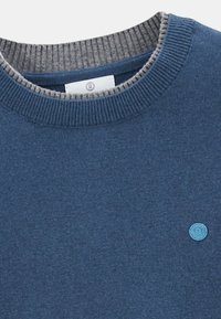 Pull bleu avec un col côtelé gris clair, présentant un petit logo circulaire bleu clair sur la poitrine. Texture douce, design décontracté.