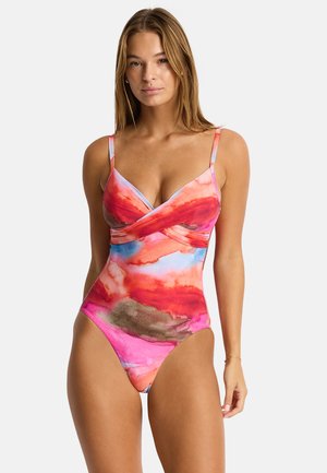 Mujer con un traje de baño de una pieza con un estampado de acuarela en rojo, rosa, azul y marrón, tirantes finos y un escote estilo cruzado.