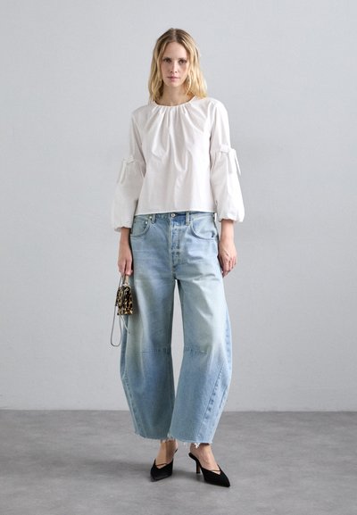 Fehér blúz puffos ujjal, világoskék, bő szárú farmer, amelynek szegélye koptatott, és fekete, hegyes orrú magassarkú cipő. Kicsi leopárdmintás táska.