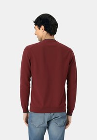 Felpa bordeaux con scollo rotondo e maniche lunghe, con polsini e orlo a costine, texture del tessuto liscia e design minimalista.