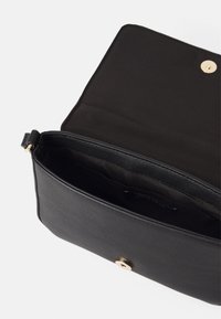 Czarna skórzana torba o gładkiej fakturze, wyposażona w złote zapięcie na zatrzask oraz pojemną wewnętrzną przegrodę wyłożoną czarną tkaniną.