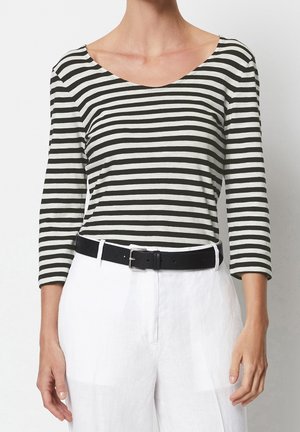 Vrouw draagt een zwart-wit gestreepte lange mouw shirt, witte hoge taillebroek en een zwarte riem met zilveren gesp.