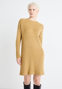 Ribbet strikket kjole i en varm beige farge, med lange ermer og noe utsvingt kant, laget av et mykt, teksturert stoff.