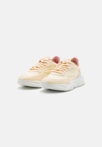 Light peach athletic shoes with a textured synthetic upper, matching laces, and rubber sole. Features a pink mesh collar and logo detail.