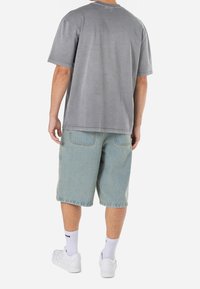 Šedé bavlněné tričko s krátkým rukávem, spárované s světle modrými denimovými kraťasy, nošené s bílými teniskami a žebrovanými sockami.