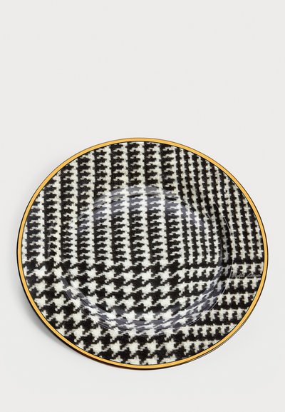 Rund keramikfat med ett svart och vitt hundtandsmönster, accentuerat med en guldrand. Slät, blank yta.