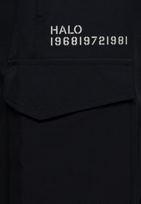 Zwarte stof met een klepzak en witte gespoten tekst met de tekst "HALO 1968 1972 1981" boven de zak.