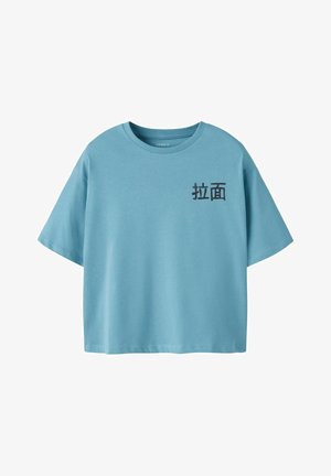 T-shirt en coton bleu clair à manches courtes et col rond. Présente un texte noir dans une police stylisée sur le côté gauche.