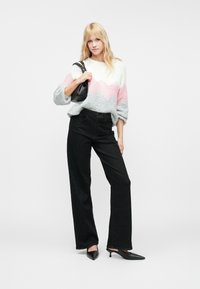 Svetr v šedé, růžové a bílé chevronové vzoru, kombinovaný s černými džíny s vysokým pasem a špičatými černými podpatky. Drží se casual kabelka.