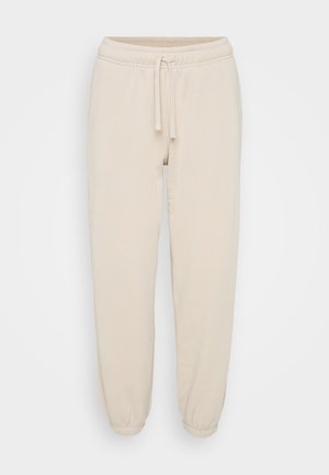 Beige bomullssweatpants med elastisk midje, snøring og elastiske mansjetter, vist på en ensfarget hvit bakgrunn.