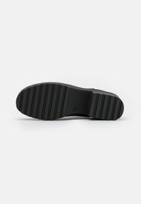 Suela de zapato de goma negra con un patrón de banda de rodadura estriada y una superficie plana. La suela presenta un logotipo grabado cerca del área del talón.