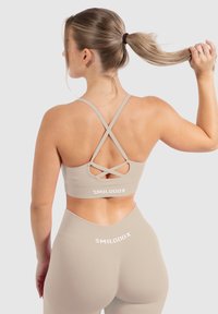 Sostén deportivo beige con correas cruzadas en la espalda, textura suave y logo en el dobladillo, combinado con leggings de cintura alta a juego.