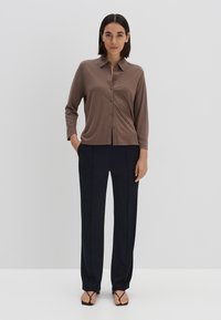 Chemise marron à manches longues avec col, associée à un pantalon large en bleu marine foncé. Tissu doux, design épuré et style minimaliste.