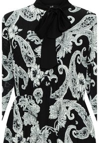 Vestido negro con patrones de paisley y flores en blanco, con mangas largas, cuello alto y un lazo en el collar. Textura arrugada.