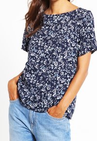 Marinblus med blommönster i ett lätt tyg, med kort ärm, rund halsringning och avslappnad passform med blåa och vita blomsterfigurer.