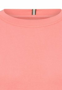 Kortærmet top i lyserød bomuld med rund halsudskæring og subtil syning. Har en stribet accent bag på nakken.