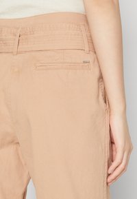 Helle rosa Hose mit einem breiten strukturierten Bund, Detail an der Gesäßtasche und weichem Stoff. Sichtbare Nähte entlang der Nähte und der Taschenlinie.