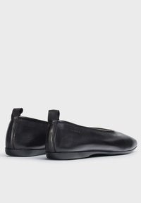 Bailarinas de cuero negro con una forma elegante, punta redondeada, costuras sutiles y una pequeña etiqueta en la parte trasera para facilitar su uso. Textura suave, diseño minimalista.