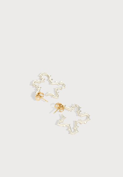 Boucles d'oreilles métalliques dorées en forme d'étoile avec des bords irréguliers et pointus et des fermoirs à poussoir sur fond blanc.