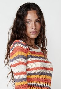 Suéter de punto multicolor con un patrón geométrico en tonos naranja, amarillo, crema y púrpura; diseño texturizado y ligero.