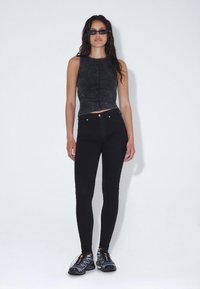 Top corto negro de tela texturizada, jeans de tiro alto negros ajustados y zapatillas deportivas negras con acentos multicolores.