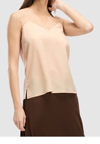 Persikkavärinen ilmanhiha-toppi, jossa on pitsiviimeistely olkapäillä. Kampaus on sileä, V-mallinen ja sivuilla on halkiot. Yhdistetty ruskeaan hameeseen.