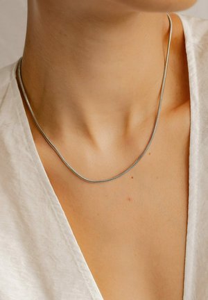 Silver snake chain necklace resting on the collarbone. Smooth texture, rounded edges, and subtle shine against a light blouse.