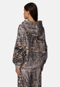 Sweat à capuche avec un motif camouflage aux nuances de brun, gris et noir. Fabriqué en tissu doux, il offre une coupe décontractée et des poignets côtelés.