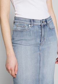 Světle modrá denimová sukně s přiléhavým pasem, designem s pěti kapsami a viditelným švem. Rovný střih s čistým lemem.