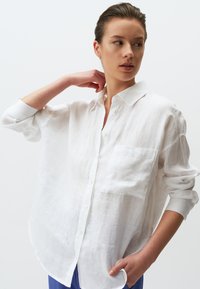 Witte linnen shirt met een casual pasvorm, knoopsluiting aan de voorkant en een enkele borstzak. Lange mouwen opgerold. Glad, lichtgewicht textuur.