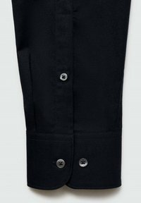 Polsino di camicia in cotone nero con due bottoni rotondi neri e una texture liscia, con una cucitura su misura e un lieve arco sul bordo.