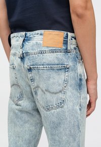 Vaqueros de mezclilla azul claro con un lavado desgastado, costuras visibles y una etiqueta de cuero marrón en la cintura con detalles de la marca.