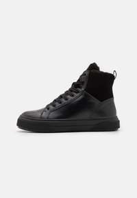 Adidași negri tip high-top cu partea superioară din piele netedă, accente din piele de căprioară, talpă din cauciuc texturat și șireturi rotunde. O bucată de prindere este la călcâi.