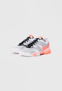 Gray athletic shoes feature a mix of smooth and textured materials, black laces, and a bright coral accent on the heel and sole.