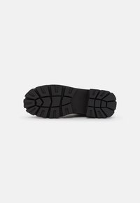 Suela de goma negra con patrones de huellas profundos para tracción; presenta un diseño sólido y flexible con detalles moldeados para una mayor durabilidad.