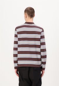 Polo de manga longa em castanho com riscas horizontais brancas e azuis claras. Apresenta um colarinho e bainha reta. Feito de um tecido suave e texturizado.