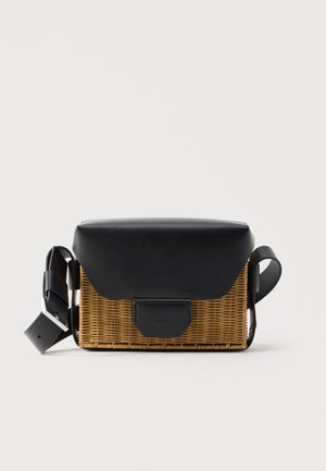 Ορθογώνια ψάθινη τσάντα χιαστί με μαύρο δερμάτινο καπάκι, μπροστινό κούμπωμα και ρυθμιζόμενο ιμάντα σε λευκό φόντο.