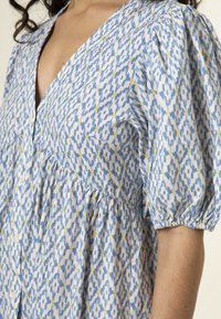 Light blue dress with a geometric pattern in darker blue and yellow. Features short puff sleeves and a deep V-neck with gathered waist.