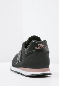 Černé textilní a kožené tenisky s kulatým tvarem, vybavené polstrovanou podrážkou, jemnými růžovými akcenty a logem 'New Balance' na patě.
