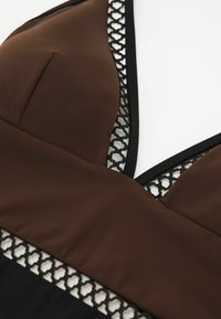 Közeli kép egy barna és fekete ruhadarabról, fekete geometrikus hálós díszítéssel a nyakkivágás és a derékrész szélén.