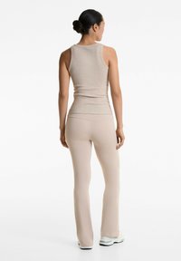 Beige gerippter Tanktop und passende enganliegende Schlaghosen, glatte Textur, Schulterträger und minimale Nähte. Abgerundet mit weißen Sneakers.