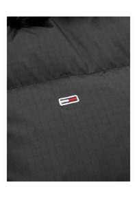 Svart jacka med rutmönster, med en liten broderad logotyp i röd, vit och blå placerad på vänster sida. Mjuk textur.
