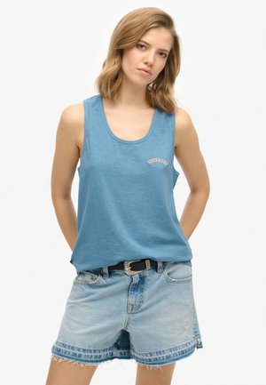 Top de algodón azul sin mangas con un escote redondo y el logo rosa de "Superdry". Combinado con pantalones cortos de mezclilla claros, con bordes deshilachados y un cinturón negro.