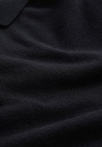 Svart tyg med en mjuk, texturerad yta; synligt vävmönster och krage detalj; slät och enhetlig yta.