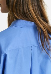 Blauwe, colbertshirt met een rugplooien in een gladde stof, met een nette afwerking en geen zichtbare hardware of accenten.