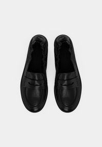 Mocassins en cuir noir avec ouvertures élastiquées, texture lisse, détails cousus et forme structurée ; design minimaliste.